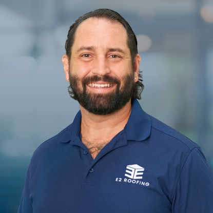 Dave Denicola, Division Manager at E2 Roofing, smiling in a blue polo shirt with the company logo, showcasing the team’s commitment to quality service and community partnership.